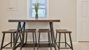 Une table à manger avec quatre tabourets, une plante en pot et une fenêtre avec des stores.