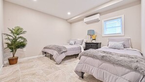 Une chambre avec deux lits, une plante en pot, une table de chevet avec une lampe et une fenêtre avec des stores.