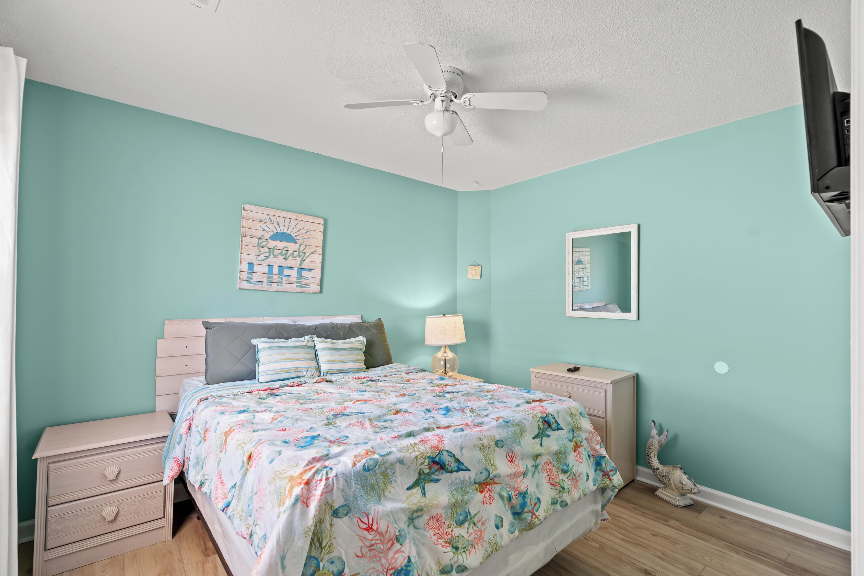 A bedroom with a bed, nightstands, a ceiling fan, a wall clock, and a decorative mirror.