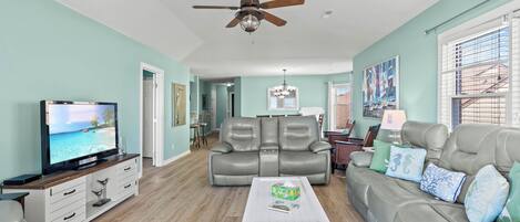 A spacious living room with a television, leather sofas, a white coffee table, and a ceiling fan.
