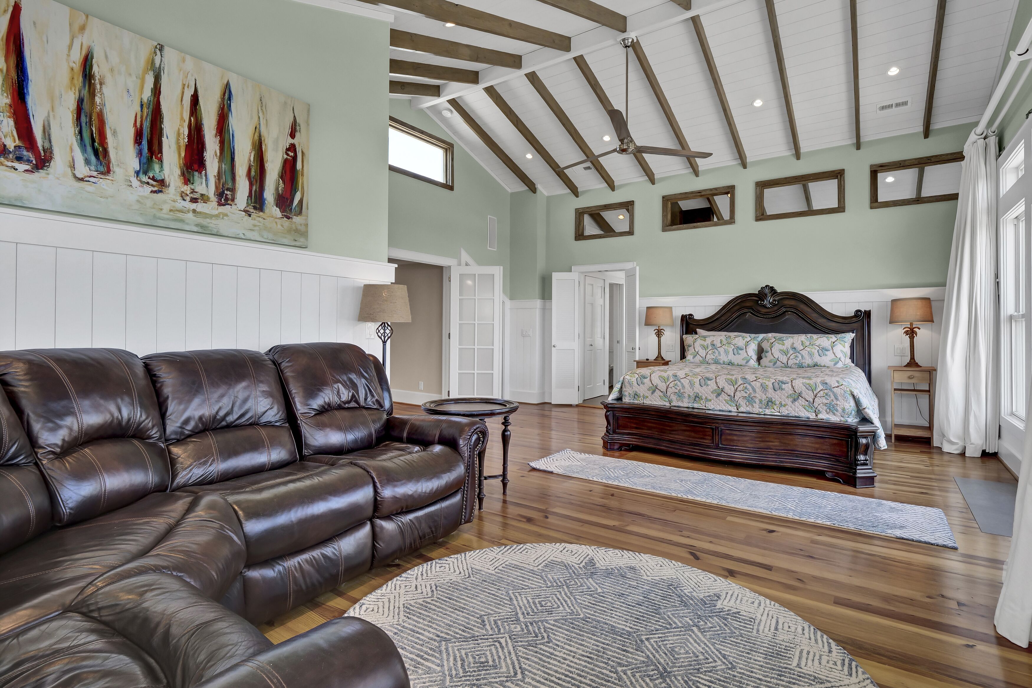 A spacious living room with a brown leather sofa, a large painting of sailboats, and a wooden ceiling.