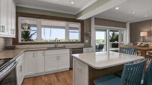 Une cuisine moderne avec des meubles blancs, un îlot central et une vue sur l’extérieur.