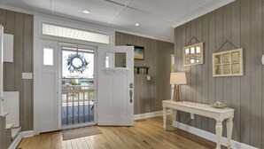 Un couloir doté d’un plancher en bois, d’une porte blanche, d’une console blanche surmontée d’une lampe, et d’objets décoratifs fixés au mur.