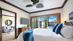 Un dormitorio con una cama grande, un ventilador de techo, un televisor y vista a un edificio desde la ventana.