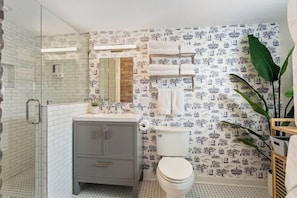 Un bagno con doccia, toilette e lavandino, caratterizzato da carta da parati decorata e una pianta.