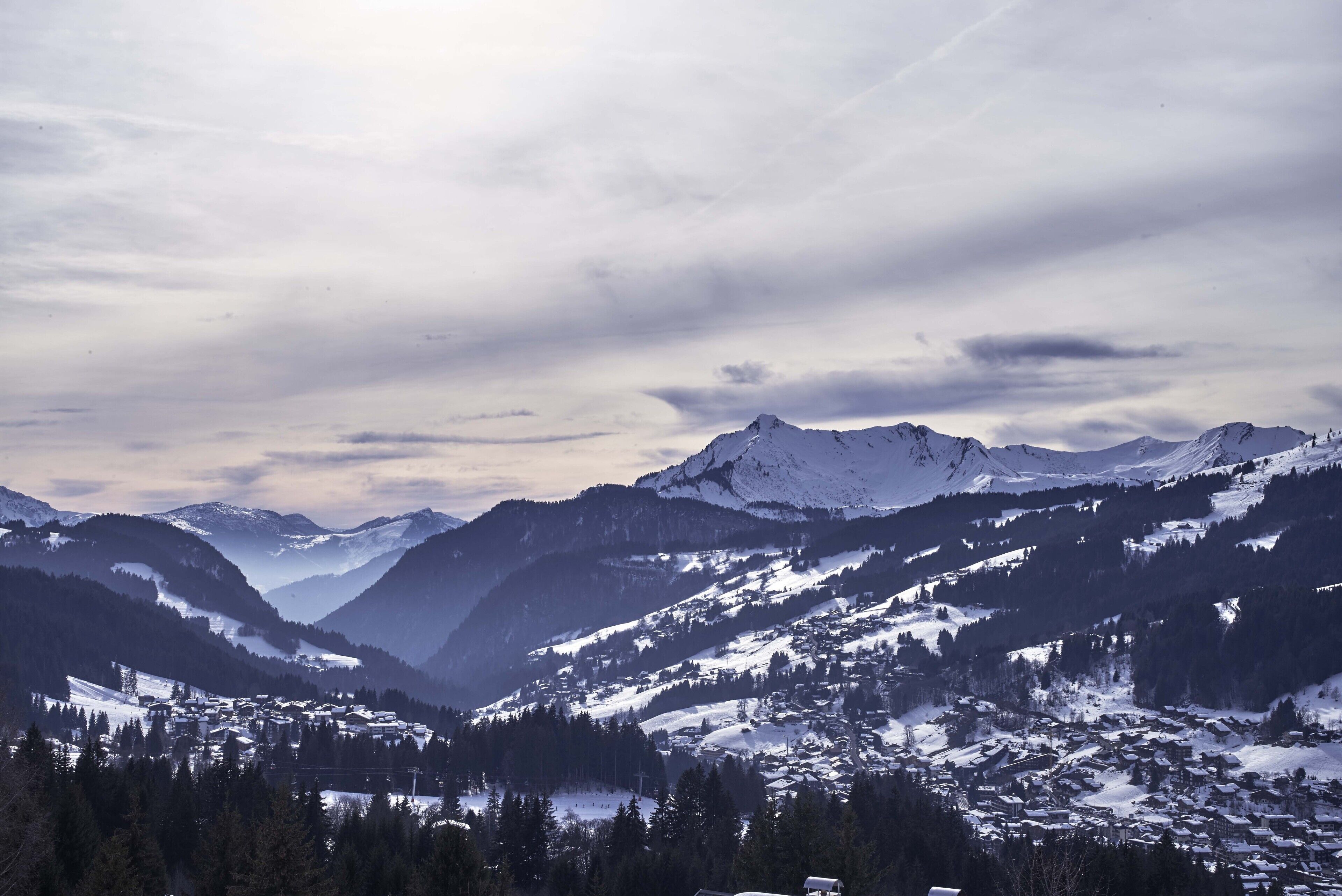Un paysage montagneux avec des sommets enneigés et une vallée parsemée de bâtiments.