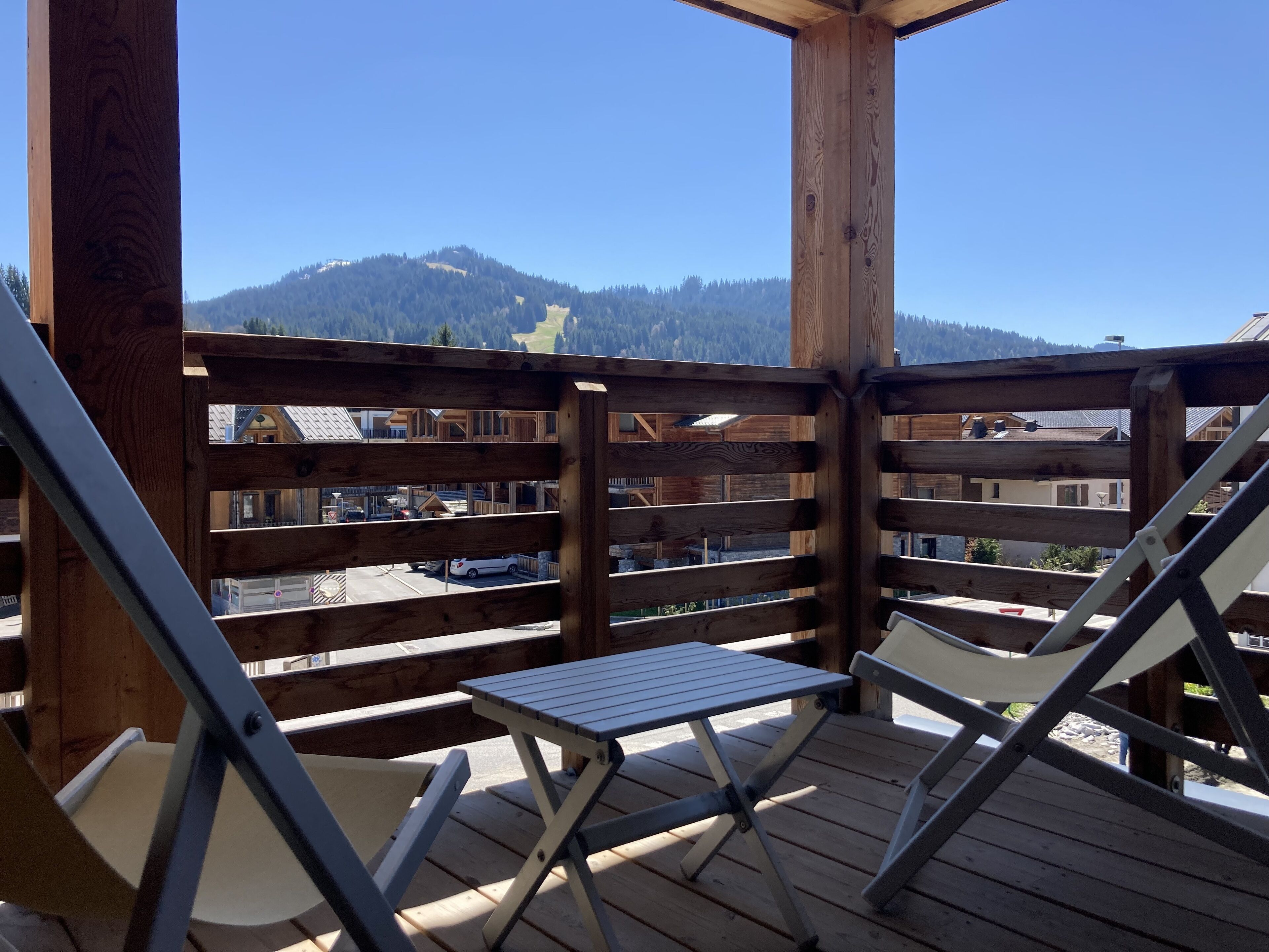 Eine Holzterrasse mit Tisch und Stühlen mit Blick auf eine gebirgige Landschaft und Gebäude.