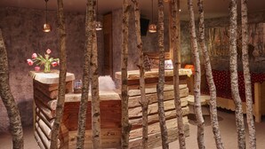Una zona de bar rústica de madera con un jarrón de flores rosadas, una pequeña mesa y lámparas colgantes.