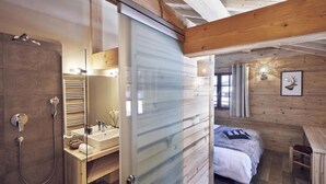 Un dormitorio de cabaña moderna con una ducha de vidrio, una cama de madera y un escritorio pequeño.