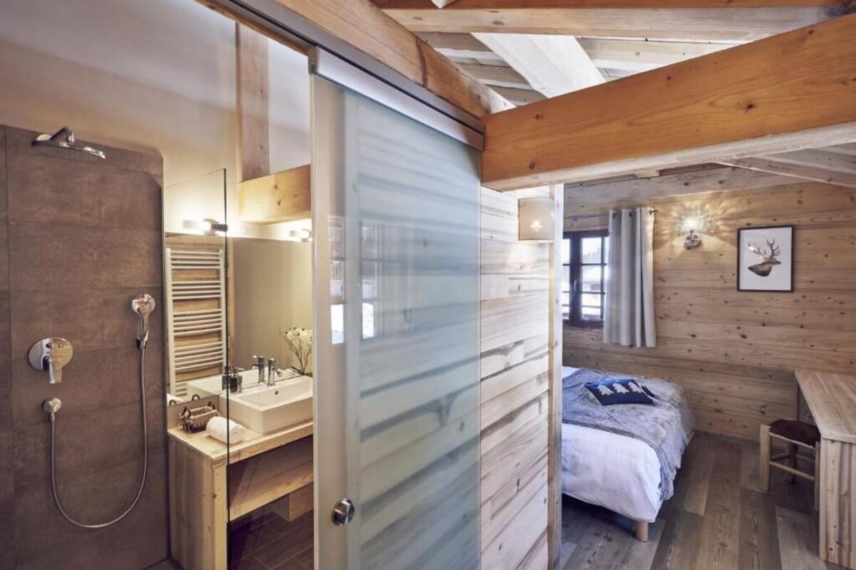 Un dormitorio de cabaña moderna con una ducha de vidrio, una cama de madera y un escritorio pequeño.