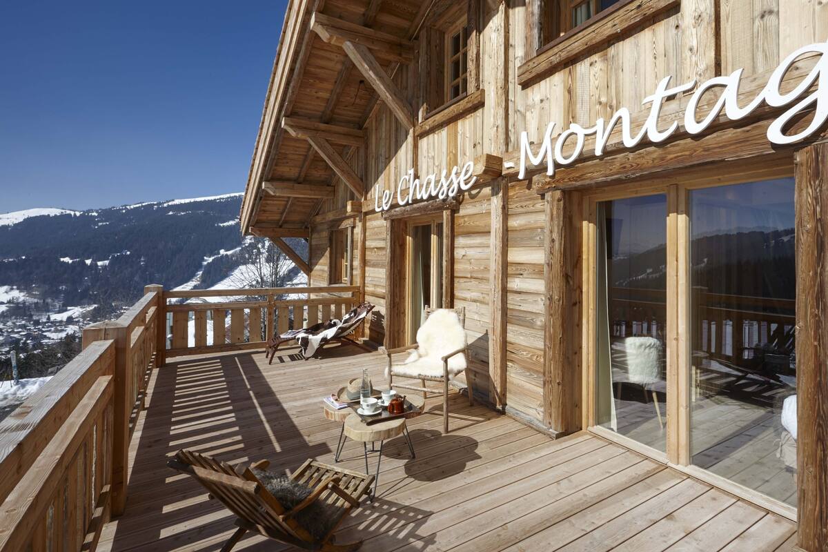Un chalé de madera con balcón que da a un paisaje montañoso cubierto de nieve.