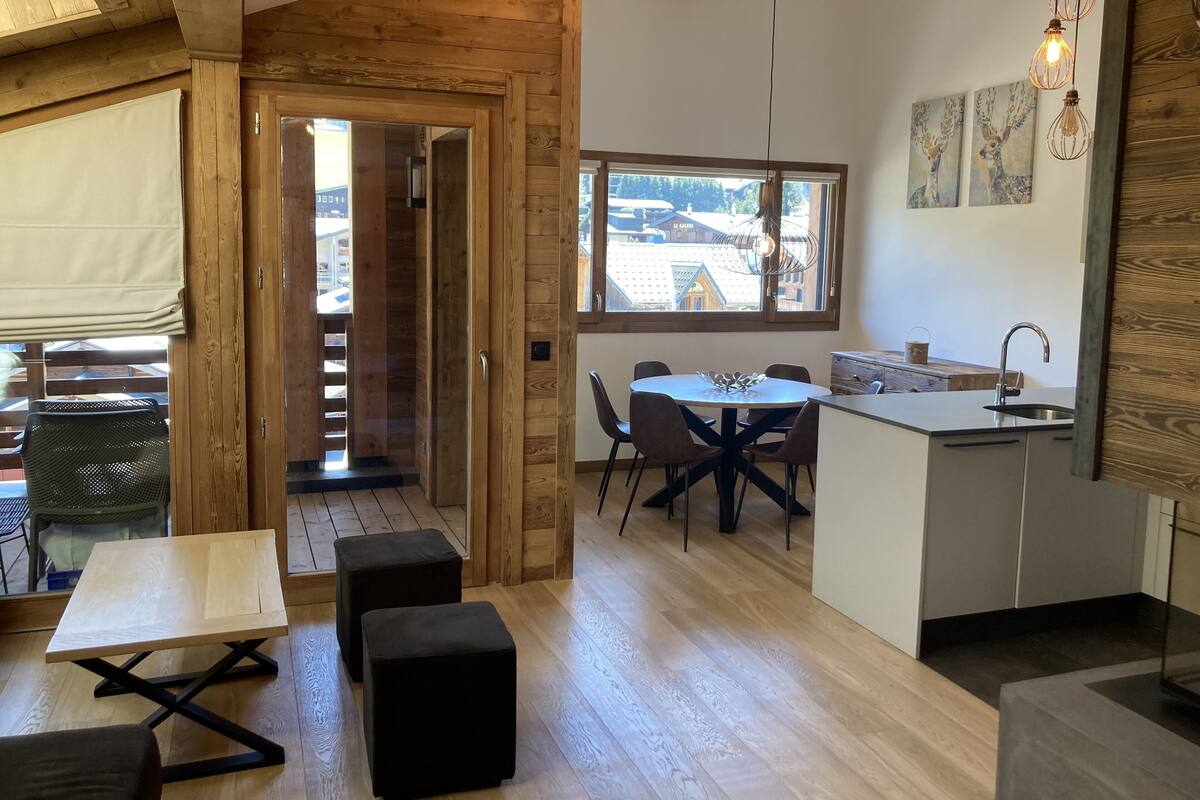 Una cocina moderna con detalles de madera, un comedor con mesa redonda y vistas al exterior a través de un amplio ventanal.