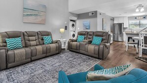 Una sala de estar moderna con dos sofás de cuero, cojines estampados, un tapete con diseño y una zona de cocina con un refrigerador y una mesa de comedor.