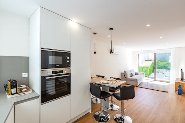 Una cocina moderna con electrodomésticos integrados, un comedor con mesa y sillas, y una sala de estar con sofá y televisor.