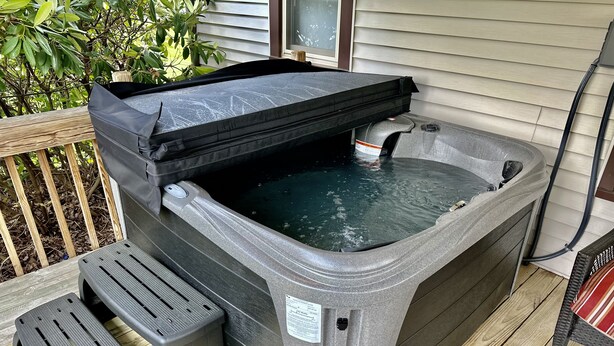 A hot tub with a control panel and a footrest on a wooden deck.
