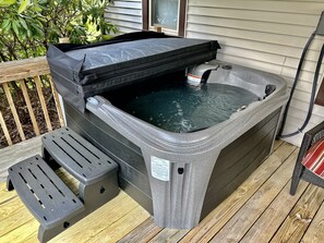 A hot tub with a control panel and a footrest on a wooden deck.