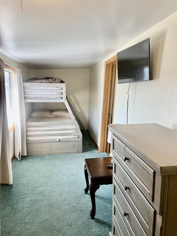 A room with a bunk bed, a dresser, and a television on the wall.