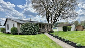 A single-story house with a porch, surrounded by well-maintained grass and a large tree.