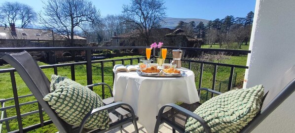 A balcony with a table set for breakfast, featuring croissants, orange juice, and a cup of coffee.