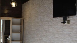A room with a stone-textured wall, a wooden bench, a radiator, and a television mounted on the wall. - Come &Rest (Kazbegi)