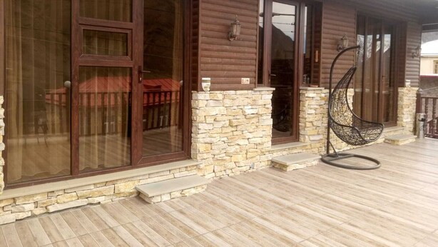 A wooden cabin with large sliding glass doors, a stone foundation, and a hanging chair on a wooden deck. - Come &Rest (Kazbegi)