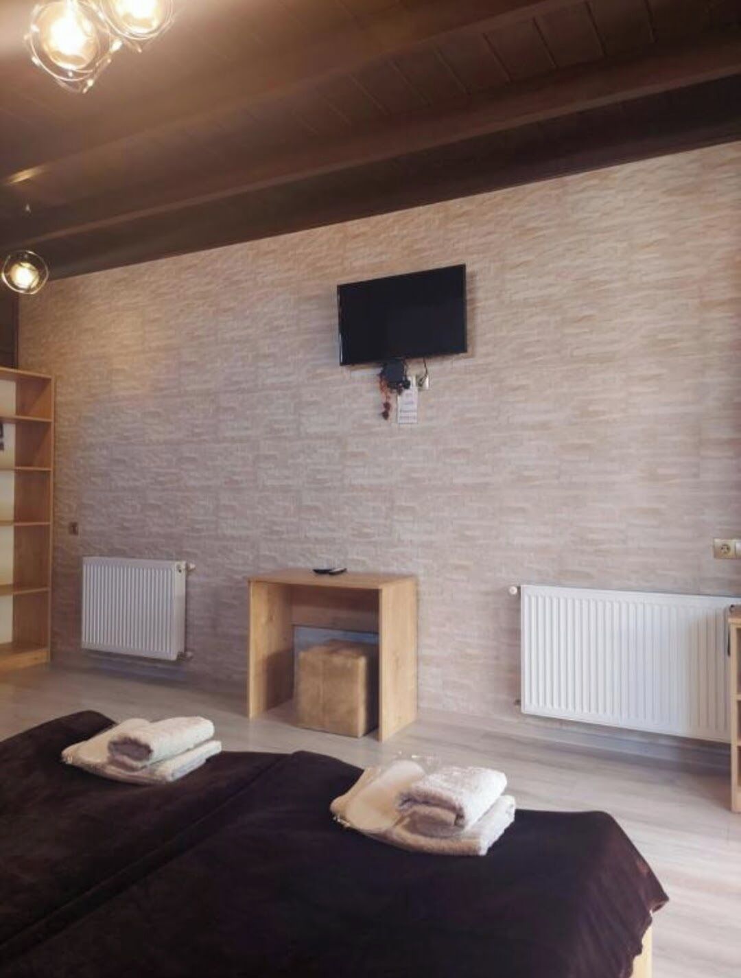 Una habitación con cama, una pequeña mesa de madera, un televisor montado en la pared y un radiador.