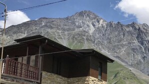 A mountain cabin with a wooden exterior and a balcony, set against a backdrop of rugged mountains and clear skies. - Come &Rest (Kazbegi)