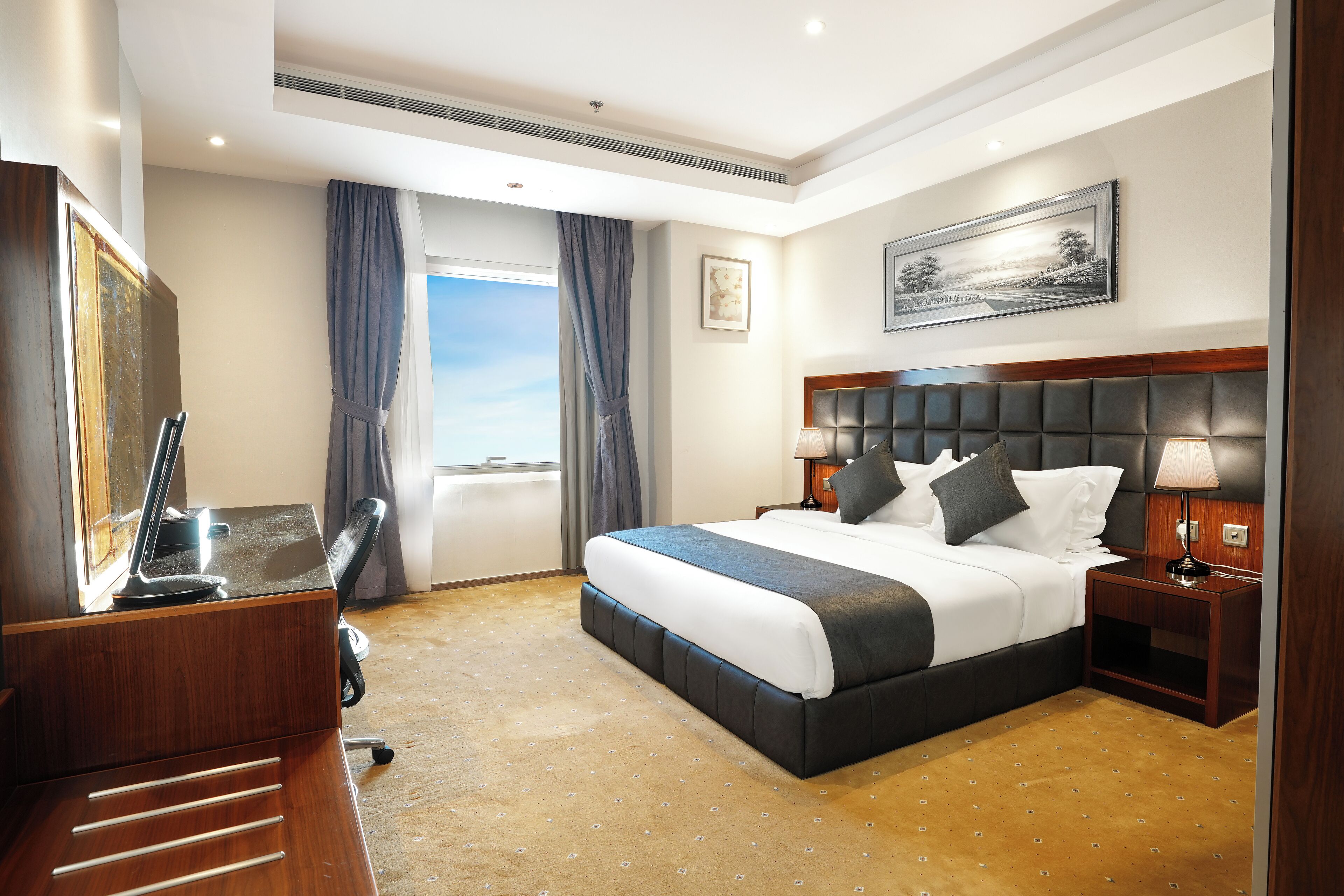 Een hotelkamer met een groot bed, een bureau met stoel, een televisie en een raam met gordijnen.