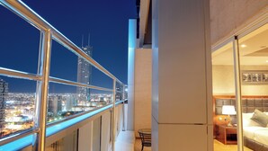 Un balcon avec vue sur la ville, une petite table avec une lampe et un lit avec une tête de lit.