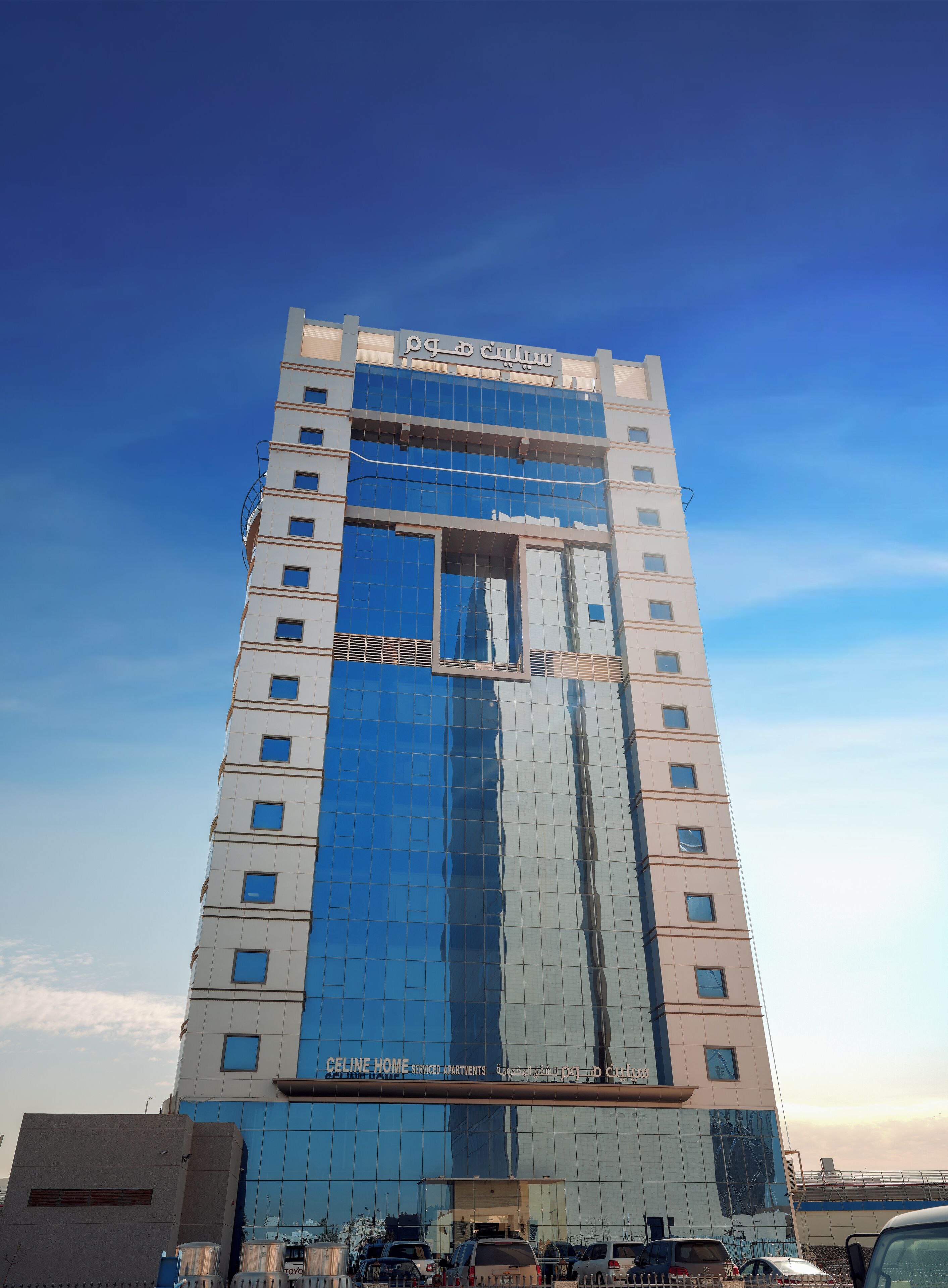 Een hoog hotel met een glazen gevel die reflecteert, meerdere verdiepingen en een opvallende entree aan de voet ervan.