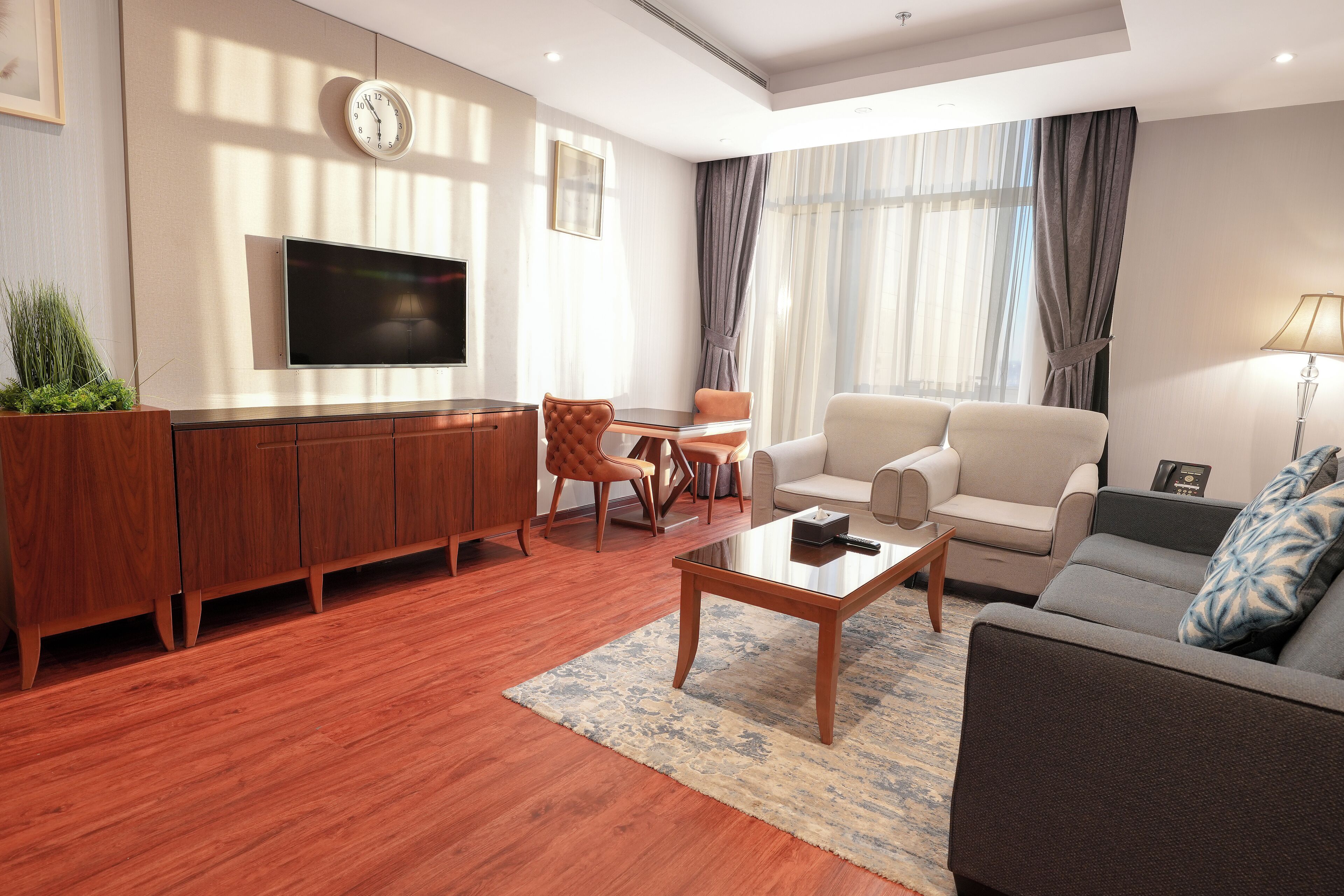 A modern living room with a flat-screen TV, wooden cabinets, a sofa, a coffee table, and a large window with curtains.