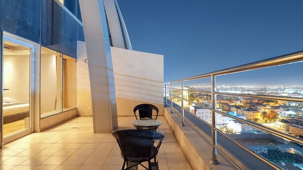 Un balcon avec deux chaises et une table, donnant sur une vue panoramique de la ville au crépuscule.