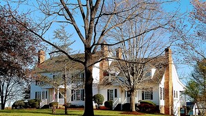 A large, two-story house with a prominent tree in front, surrounded by a well-maintained lawn.