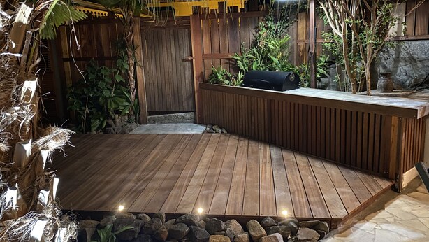A wooden deck with a built-in barbecue grill, surrounded by tropical plants and a wooden fence. - La Villa d'à Côté (Le Marin)