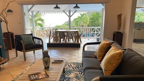 A spacious living area with a sofa, chairs, a coffee table, and a view of an outdoor patio with a table and chairs. - La Villa d'à Côté (Le Marin)