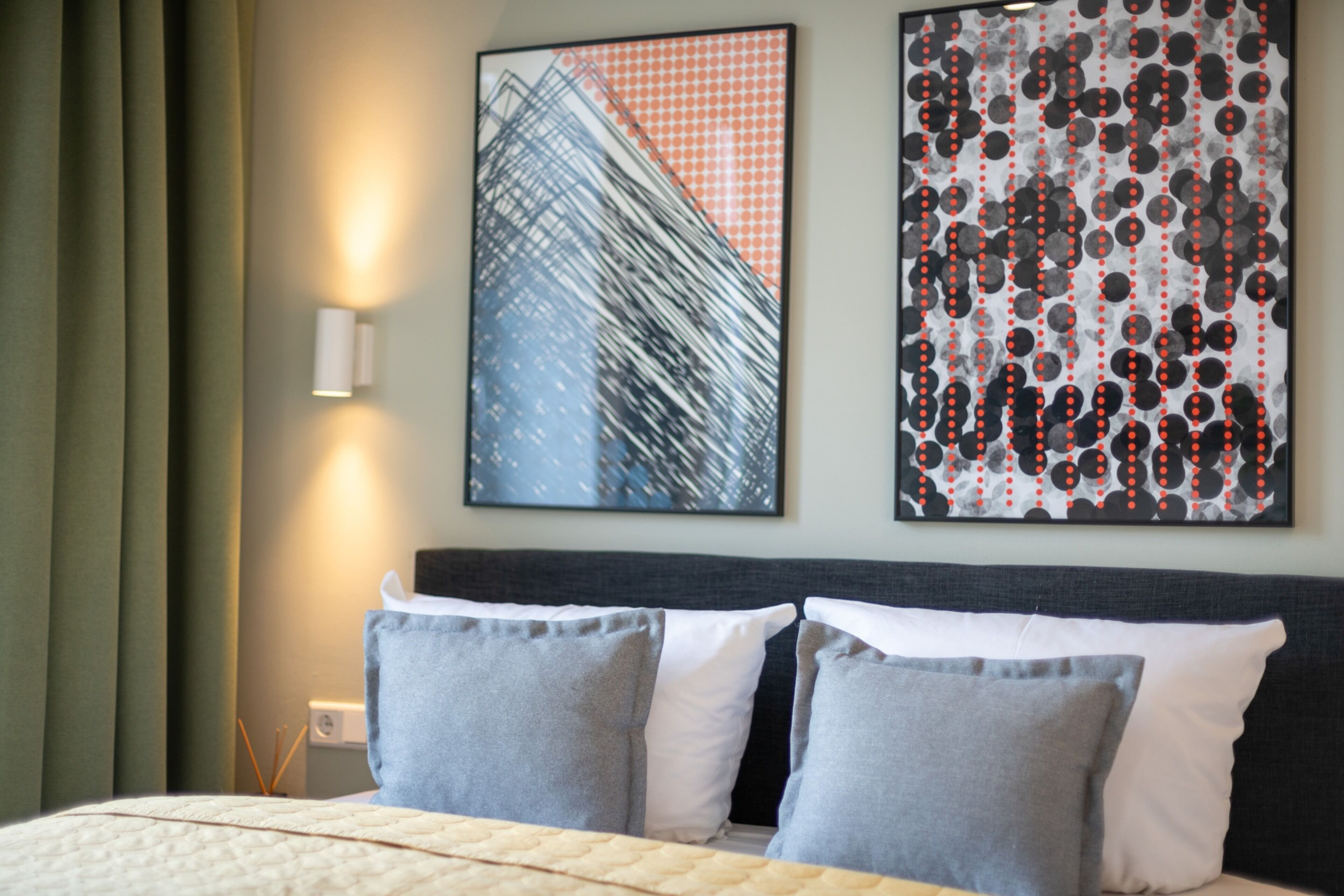 A hotel room with a bed, two pillows, a wall-mounted light, and two framed artworks.