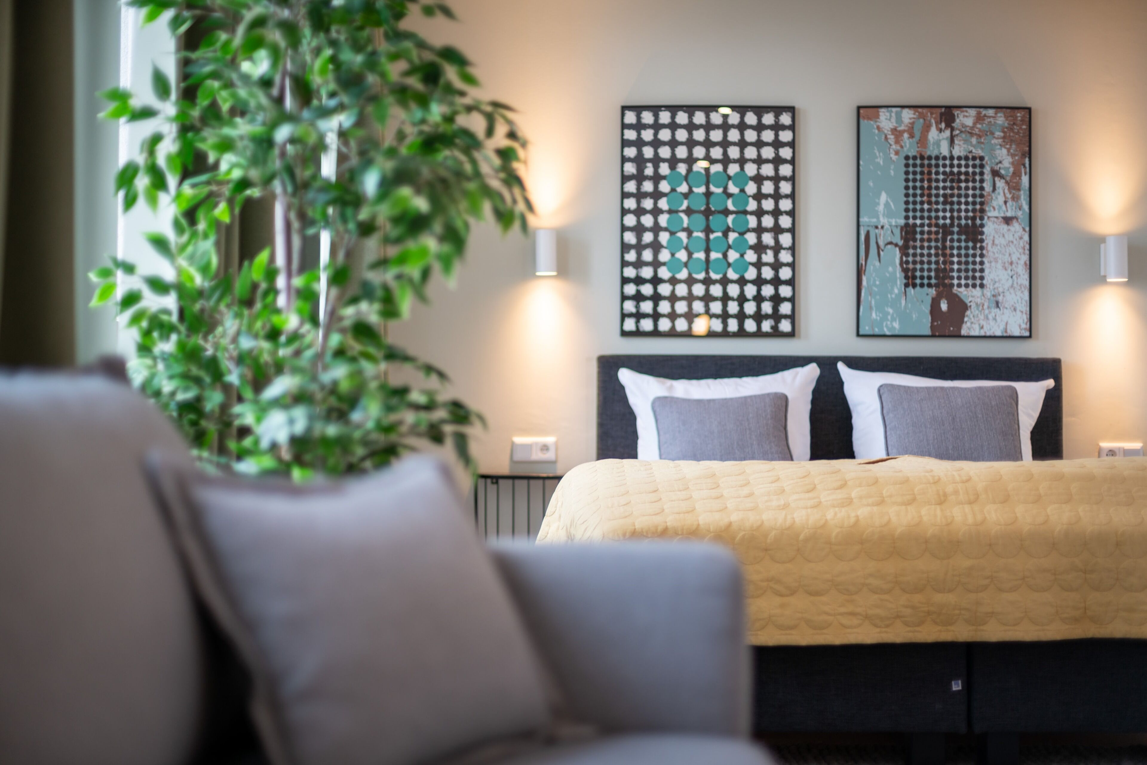 Une chambre à coucher comprenant un lit, deux lampes fixées au mur et deux œuvres d’art abstraites.