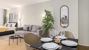 A modern hotel room with a dining area, a grey sofa, a small side table, and a potted plant. - BRIGHT Dortmund City Center (Dortmund)
