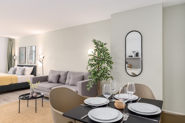 A modern hotel room with a dining area, a grey sofa, a small side table, and a potted plant. - BRIGHT Dortmund City Center (Dortmund)