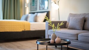 A modern hotel room with a bed, sofa, and a coffee table with a vase of flowers. - BRIGHT Dortmund City Center (Dortmund)