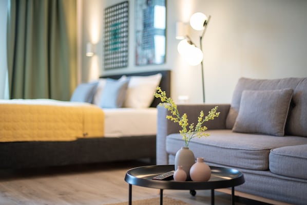 A modern hotel room with a bed, sofa, and a coffee table with a vase of flowers.