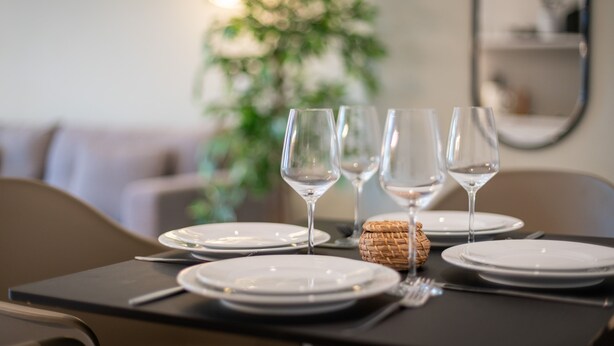 A dining table set with white plates, clear wine glasses, and a woven basket. - BRIGHT Dortmund City Center (Dortmund)