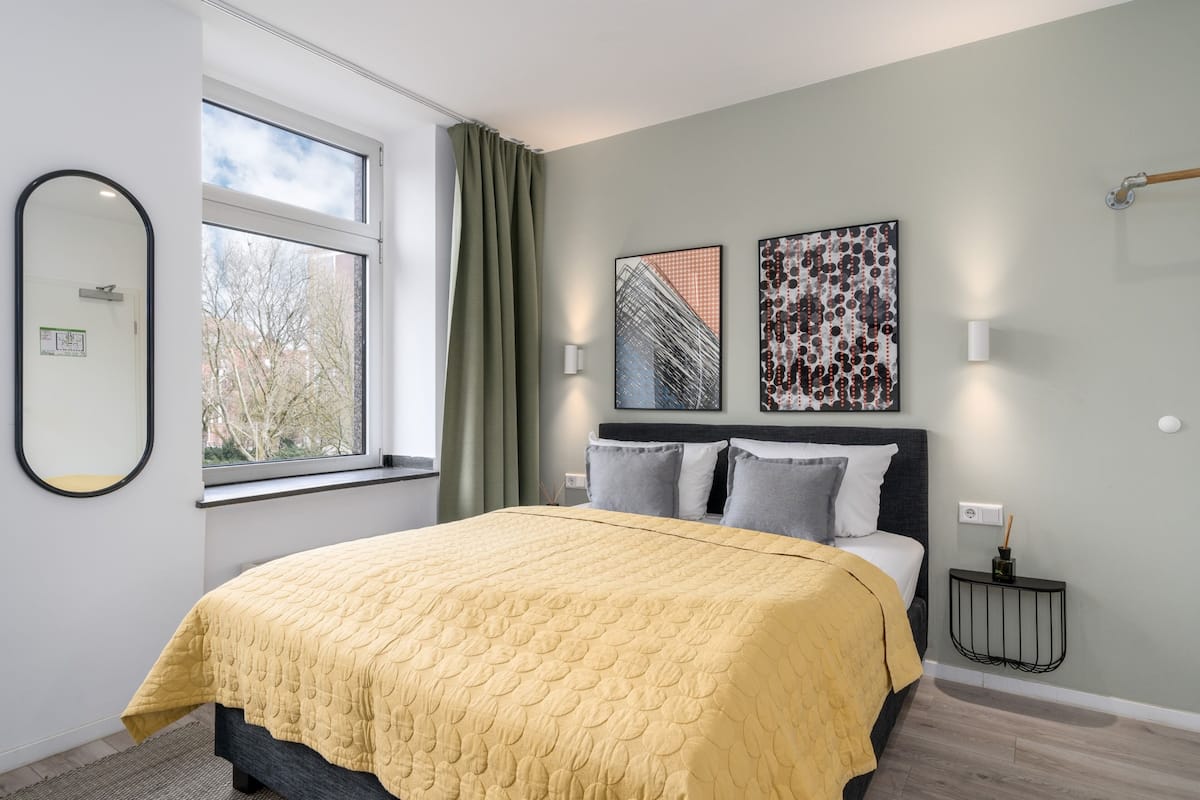A modern bedroom with a large bed, a window with curtains, and two wall-mounted artworks.