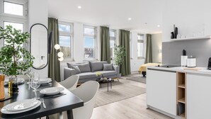 A modern living room with a grey sofa, dining table set with plates and glasses, and a kitchen area with a counter and shelves. - BRIGHT Dortmund City Center (Dortmund)