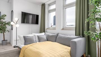 Une chambre à coucher moderne avec un lit, une télévision et une fenêtre avec des rideaux.