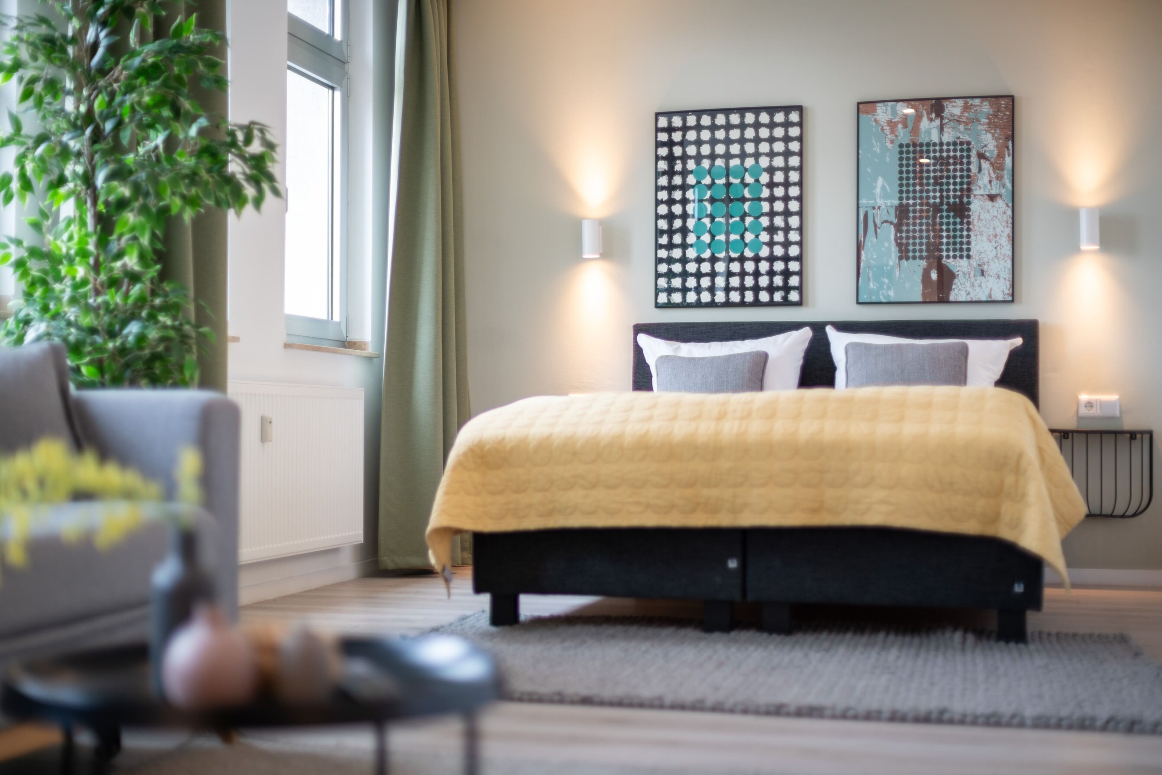 A bedroom with a bed, a chair, a plant, and artwork on the wall.