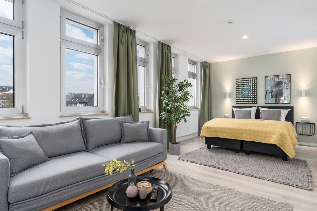 A modern living room with a grey sofa, a yellow bed, a potted plant, and artwork on the walls.