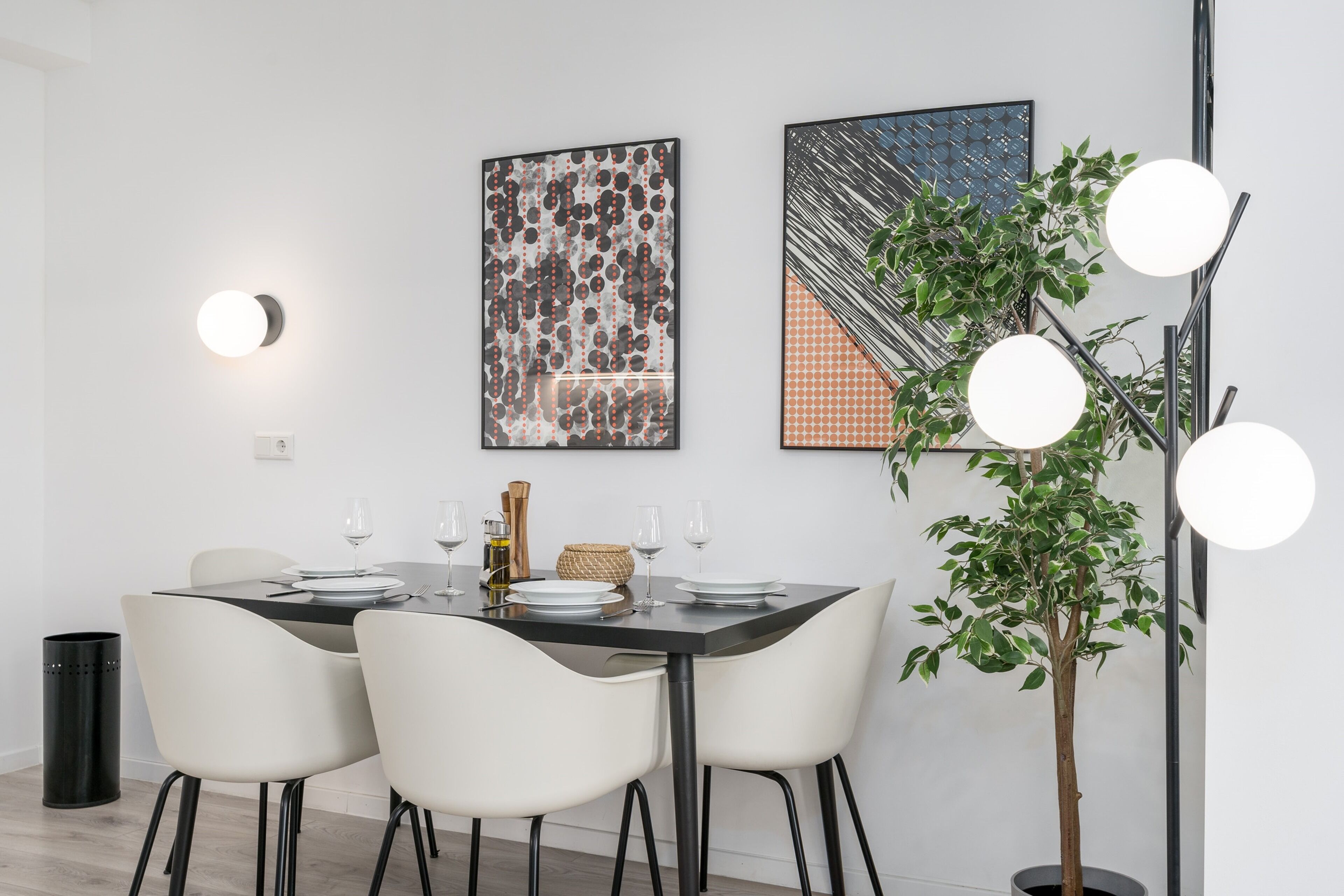 Ein Essbereich mit einem Tisch für vier Personen, weißen Stühlen, einem Blumentopf und zwei gerahmten Kunstwerken an der Wand.