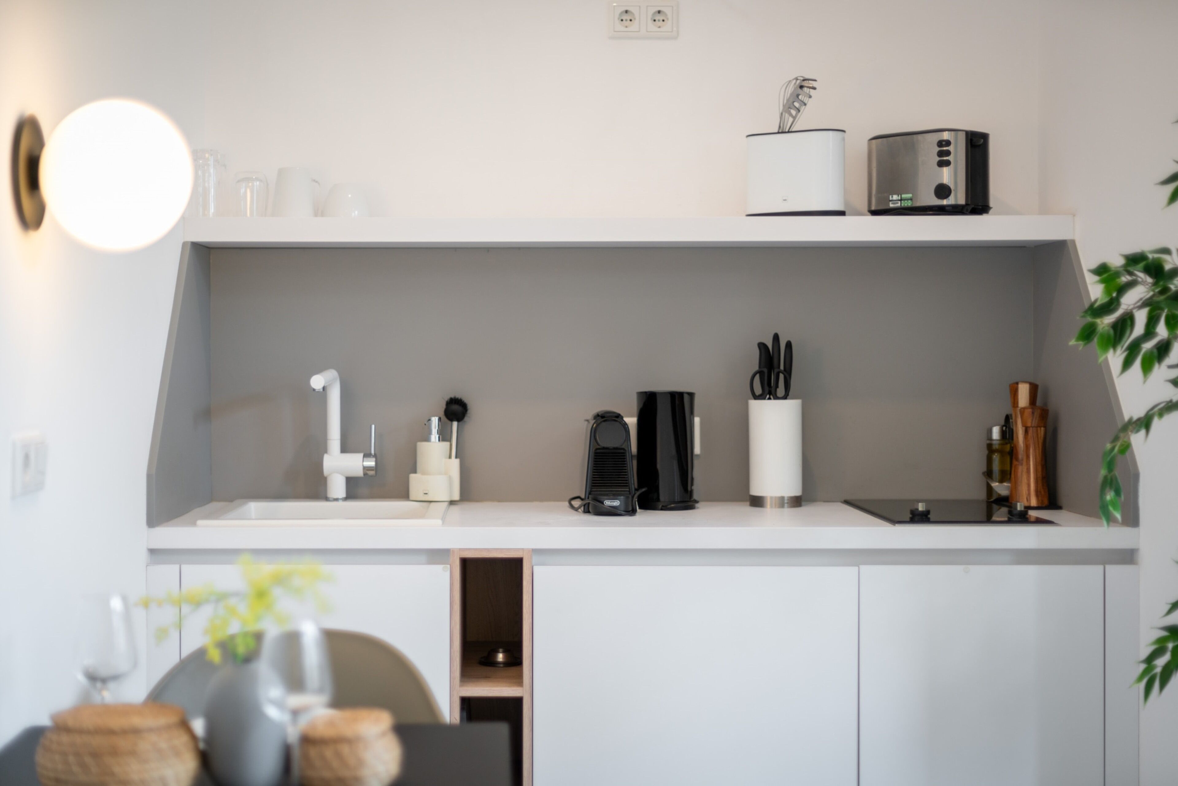 A modern kitchen with white cabinetry, a built-in coffee machine, and a small plant on the counter.