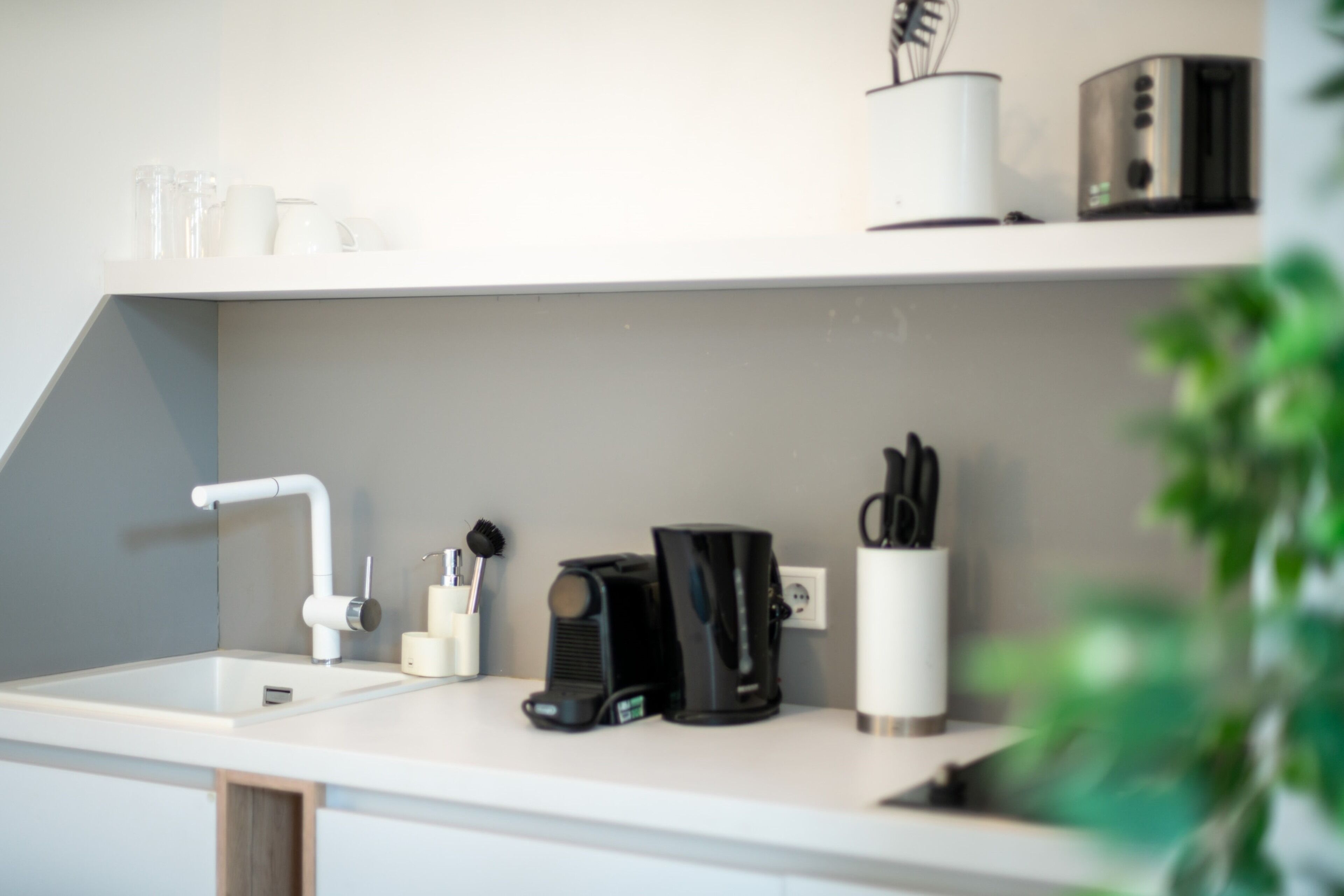 A modern kitchen with a white countertop, a coffee maker, a toaster, and a sink.